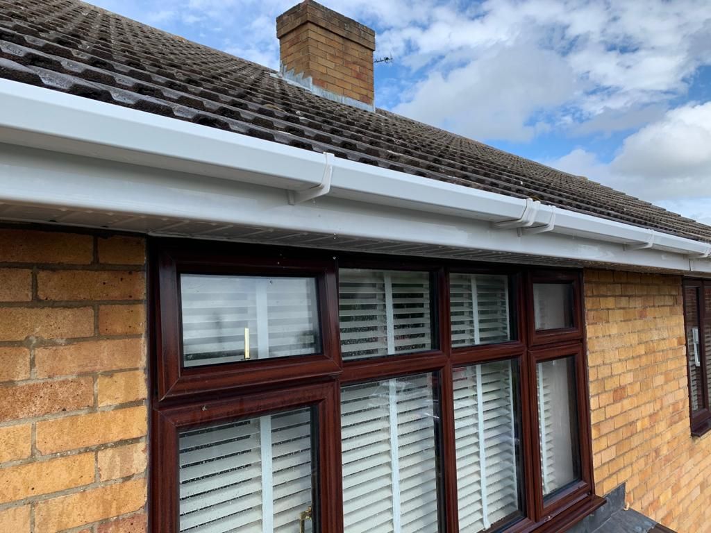 Brick house with brown window frames, white gutters, and a tiled roof against a cloudy sky.