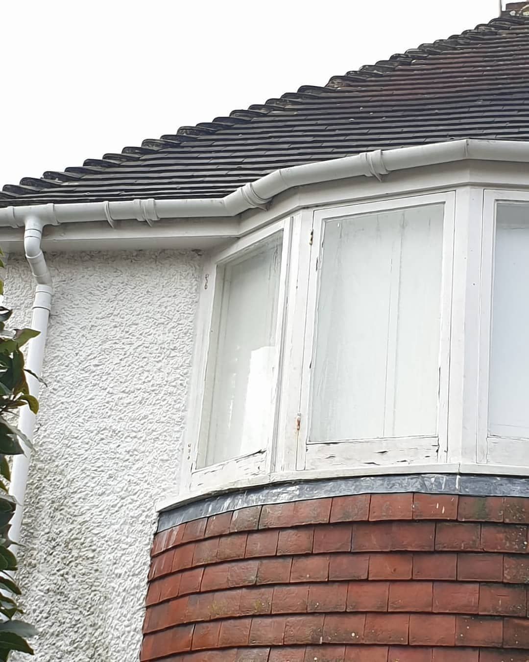 Bay window with white trim, brick base, and a tiled roof on a house exterior.