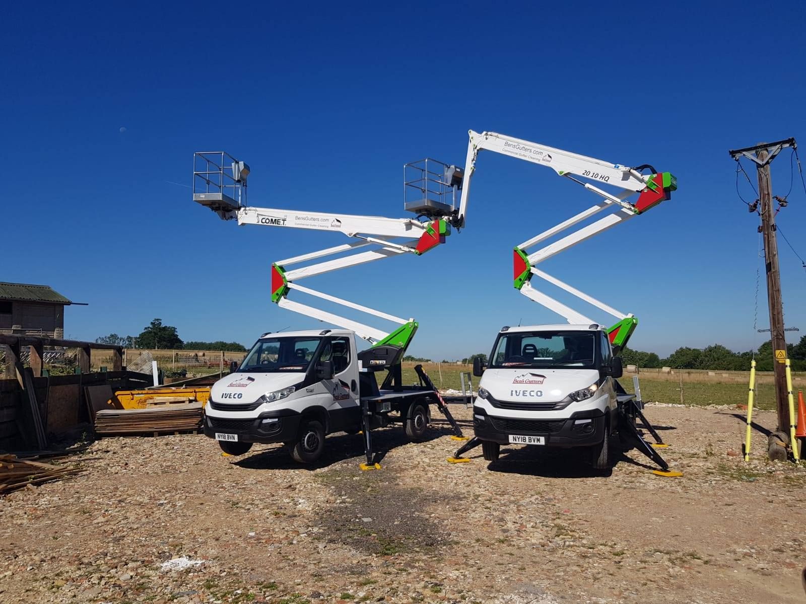 Two white work trucks with raised aerial lifts against a clear blue sky.