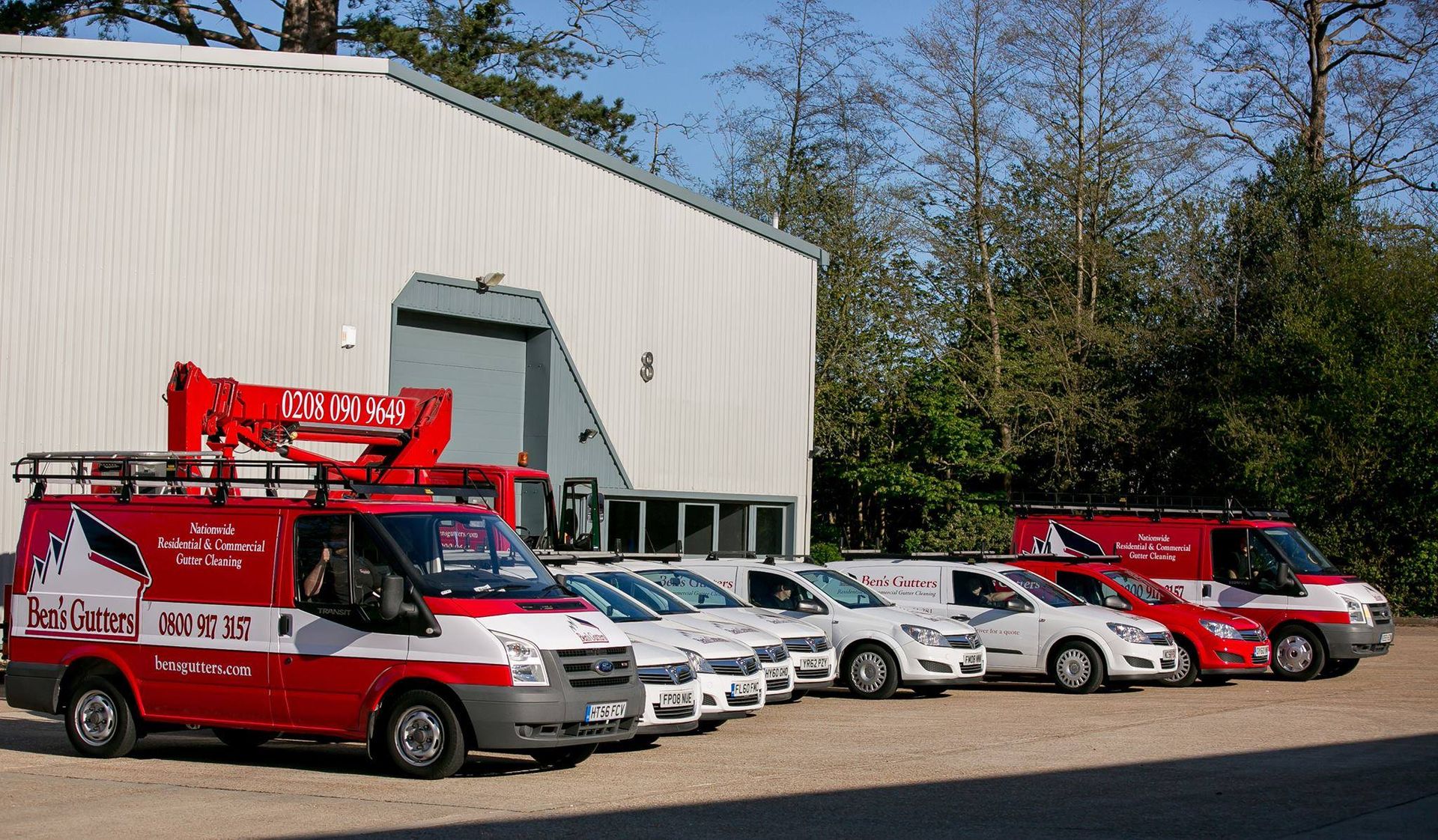 Lineup of red and white service vans in front of a white building. One van has a boom lift.