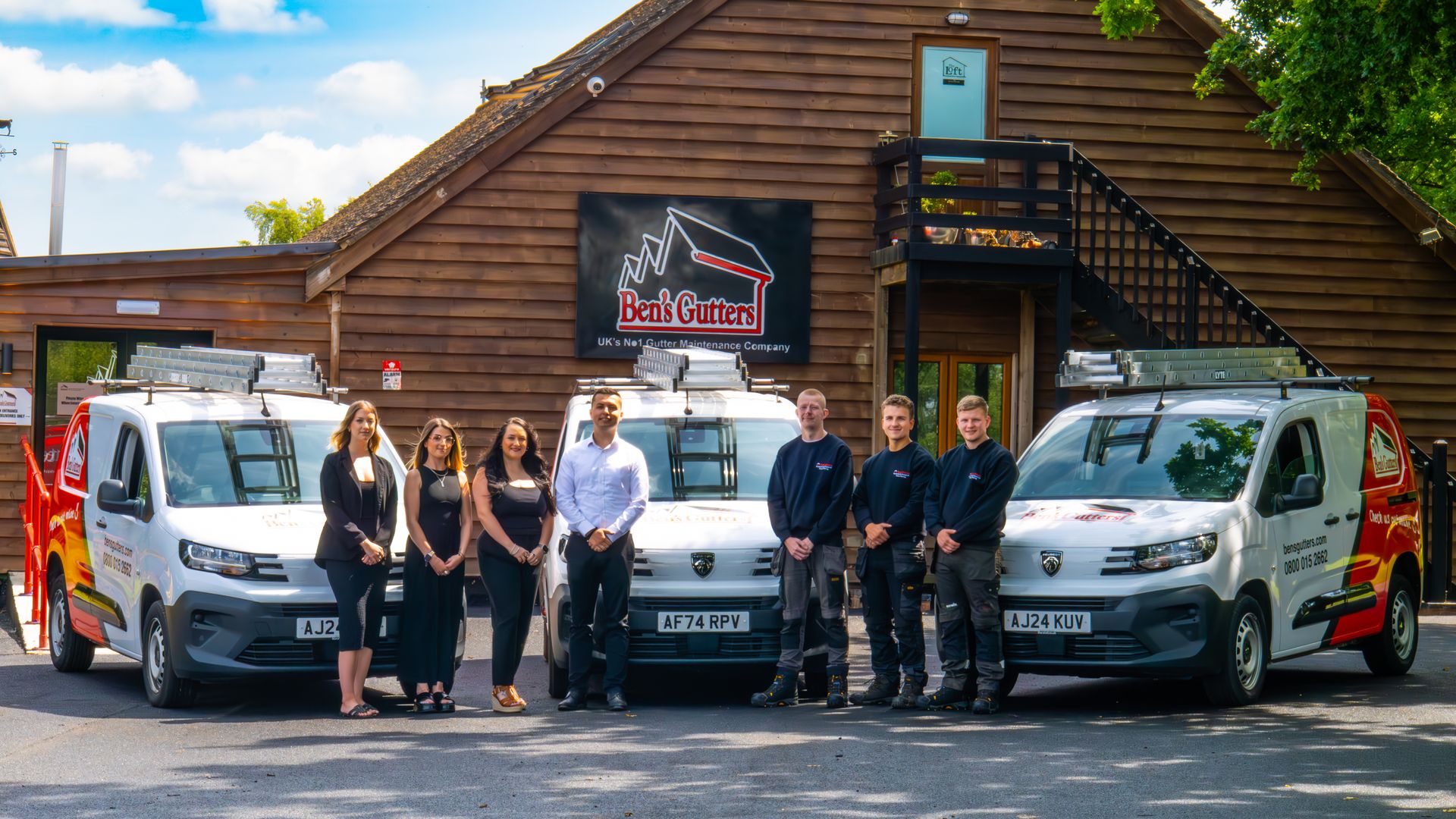 Group of people standing in front of vans and a building with a company logo.