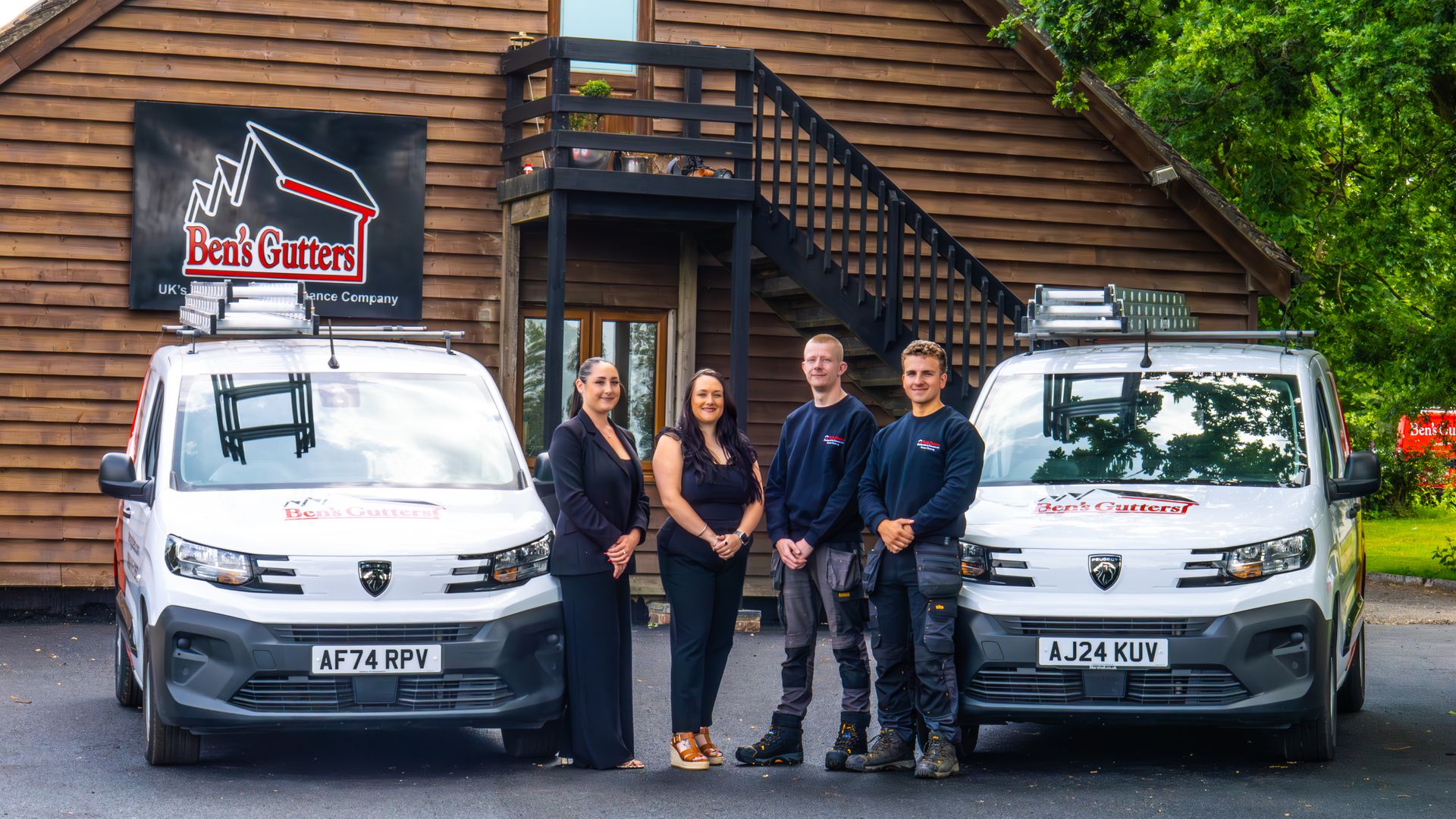 Two vans and four people in front of a building. The vans have company logos. People are smiling.
