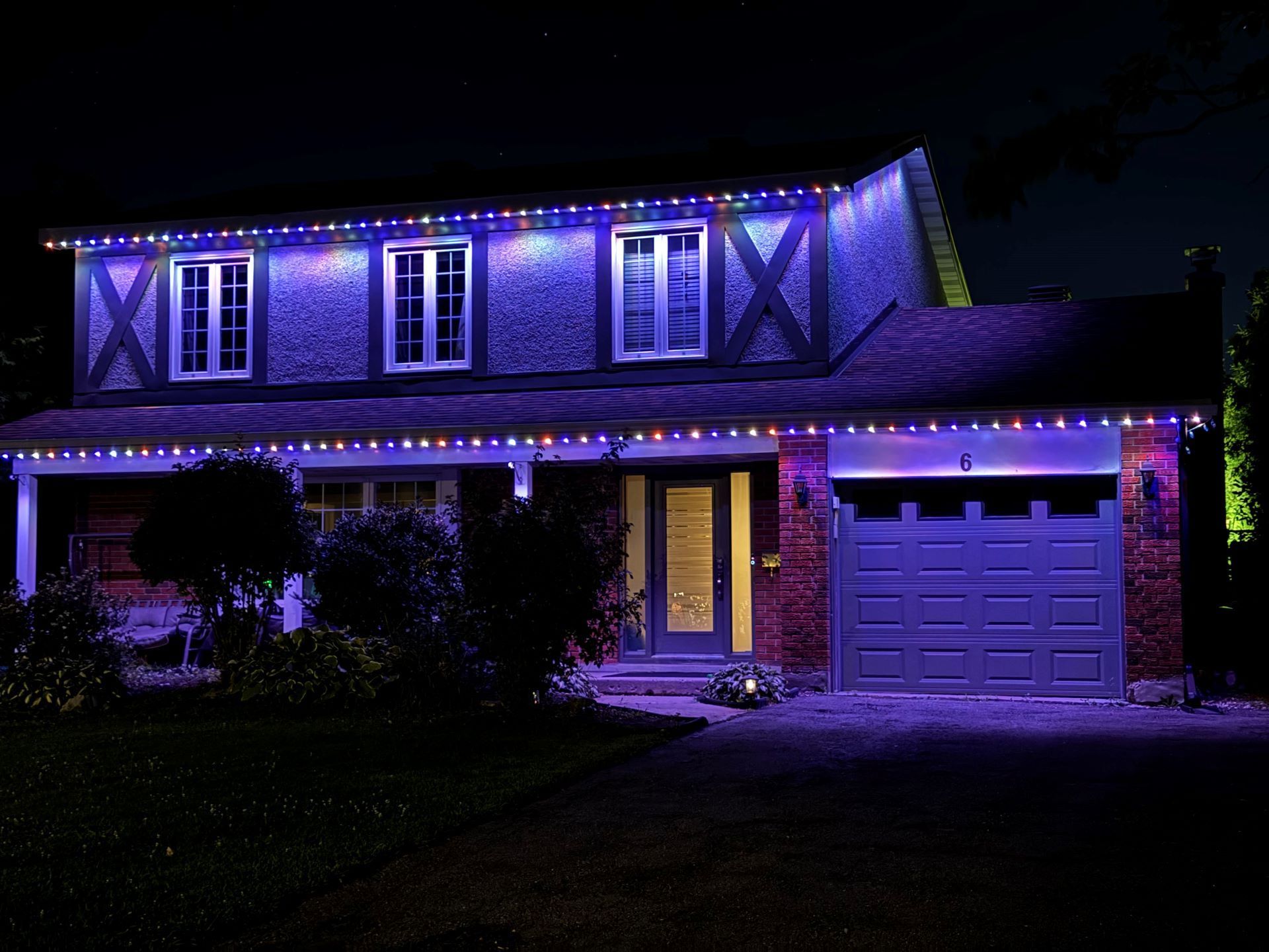 House lit with purple holiday lights at night, with a glowing porch and garage.