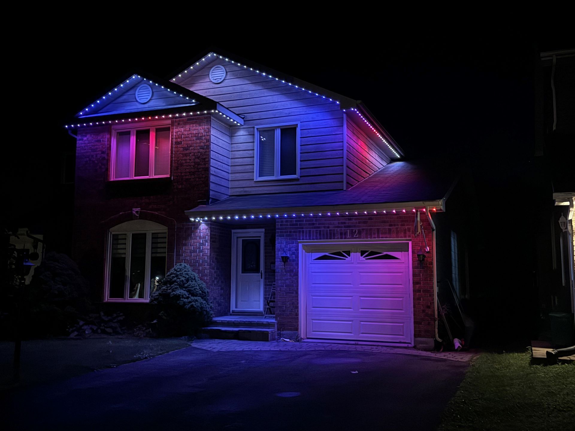 Two-story brick house at night lit with blue and pink accent lights