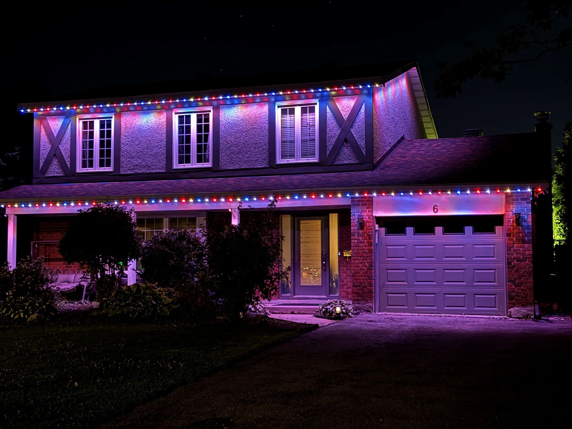 House lit with purple and pink decorative lights at night, with a garage on the right
