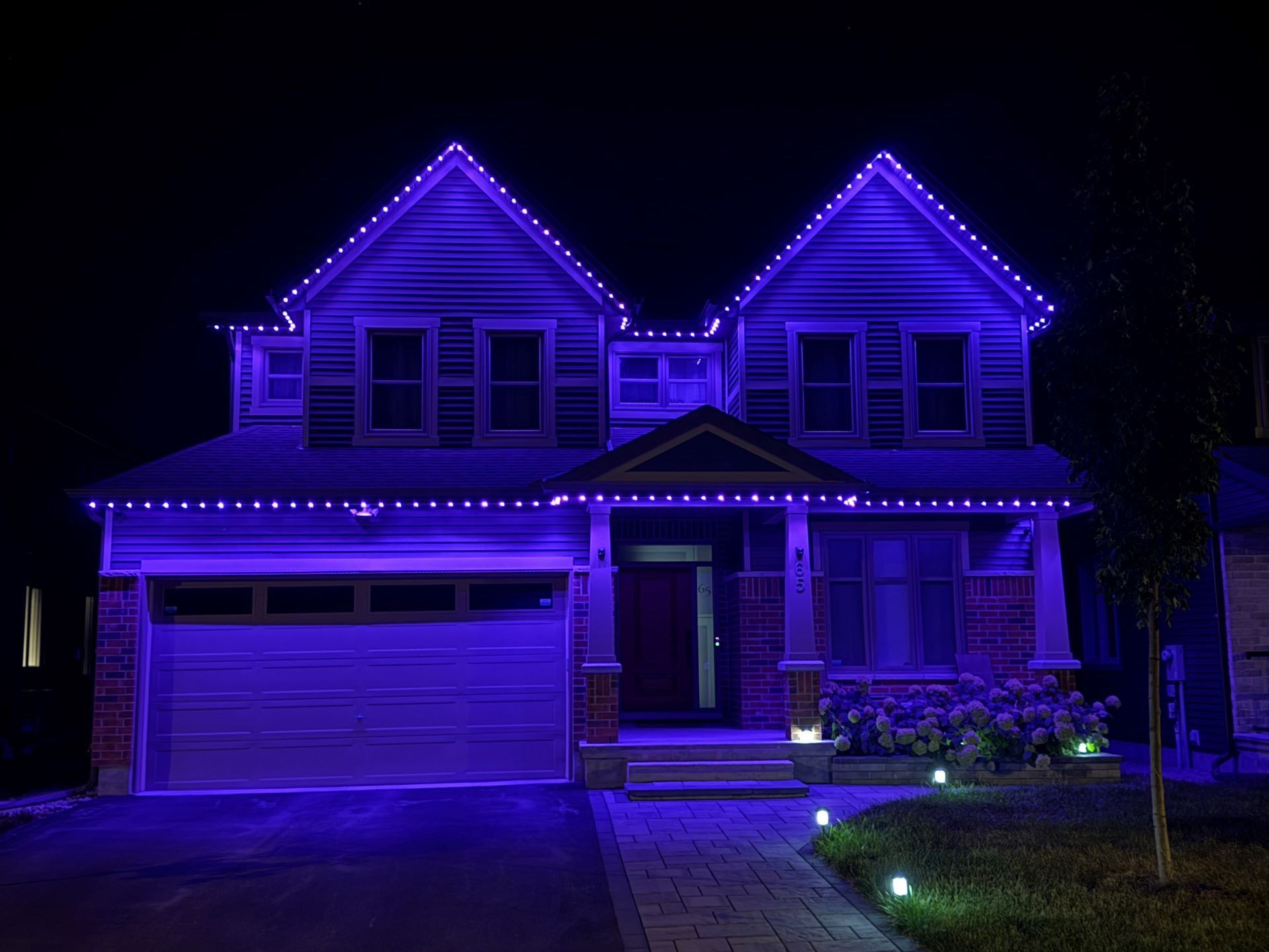 Two-story house lit with purple lights at night, with a garage and front yard path
