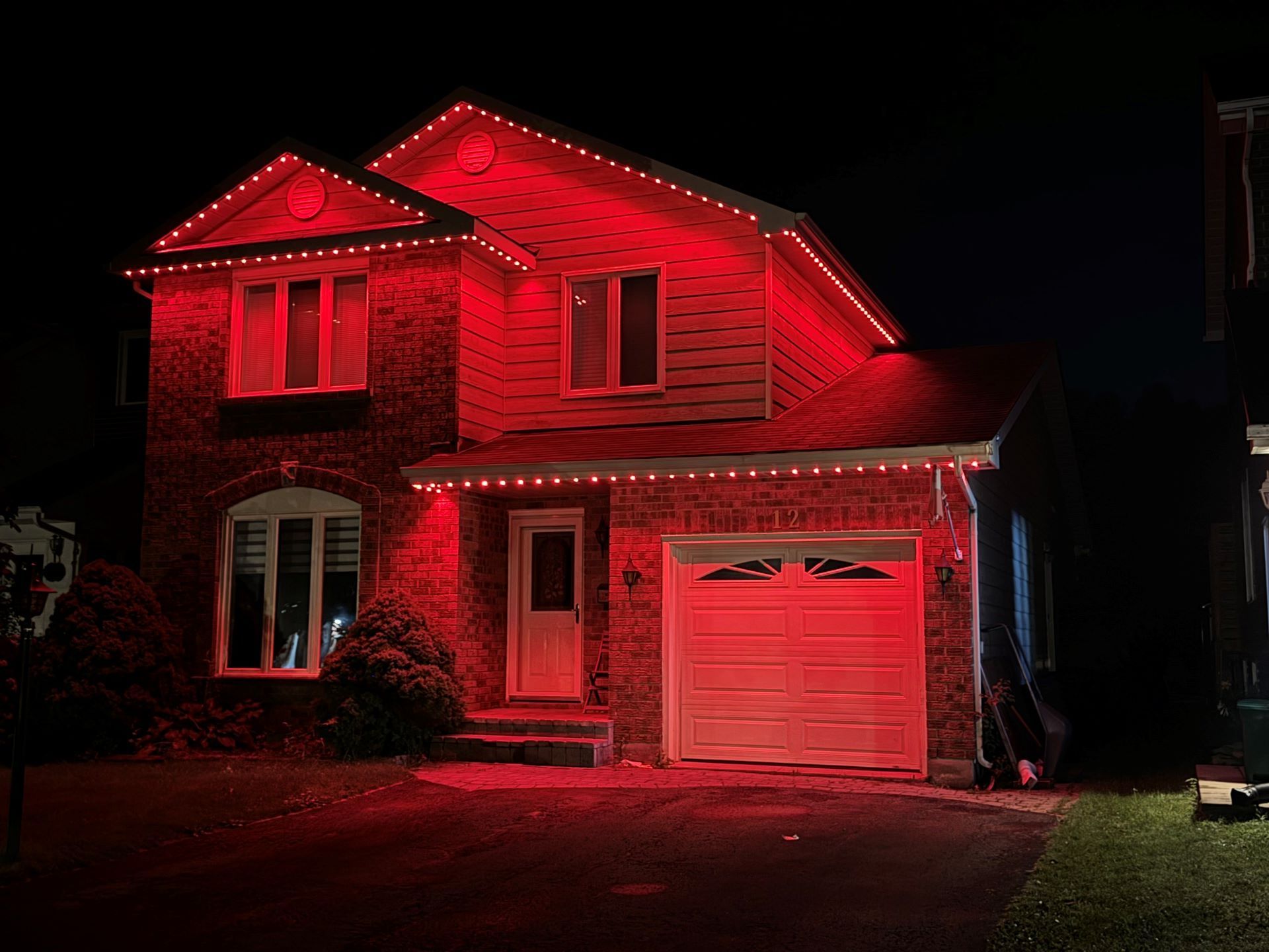 Two-story house lit with red holiday lights at night