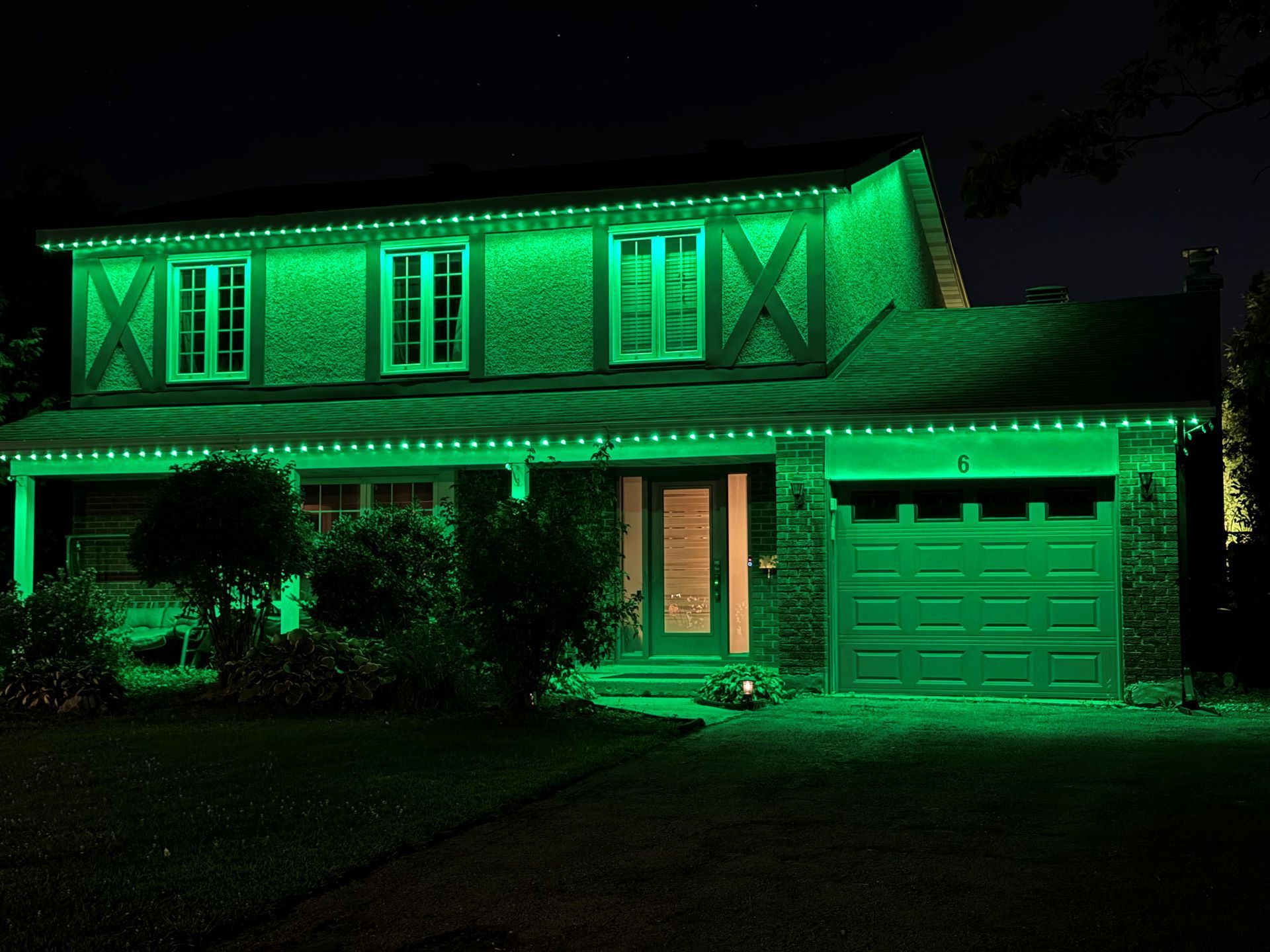 Two-story house lit with bright green lights at night, with a garage and front porch.