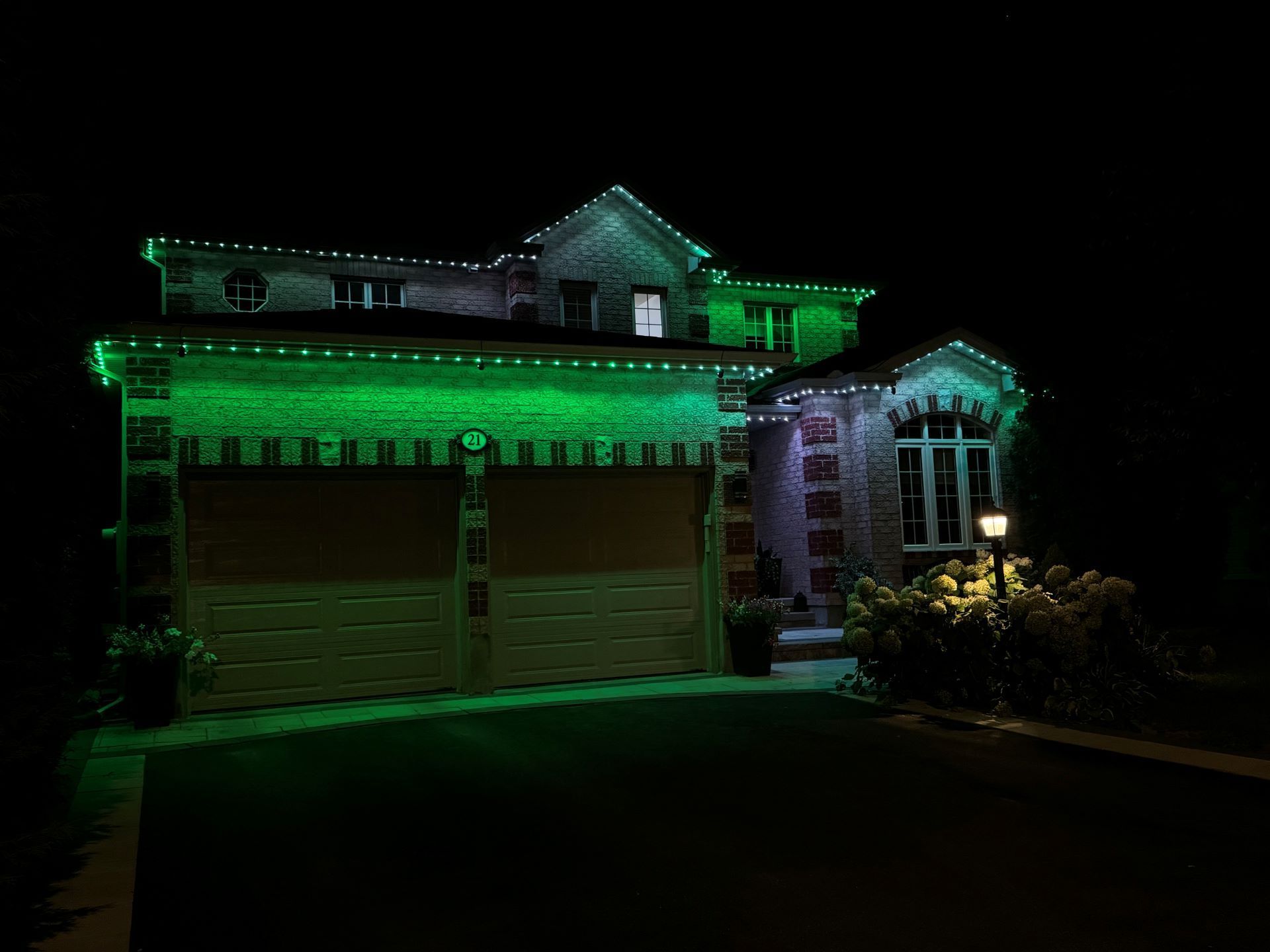 Suburban house at night lit with green holiday lights, garage and front porch visible.