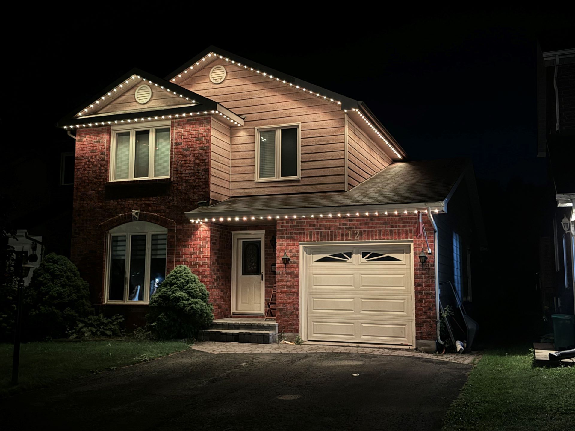 Two-story brick house at night with lights on and a garage door visible