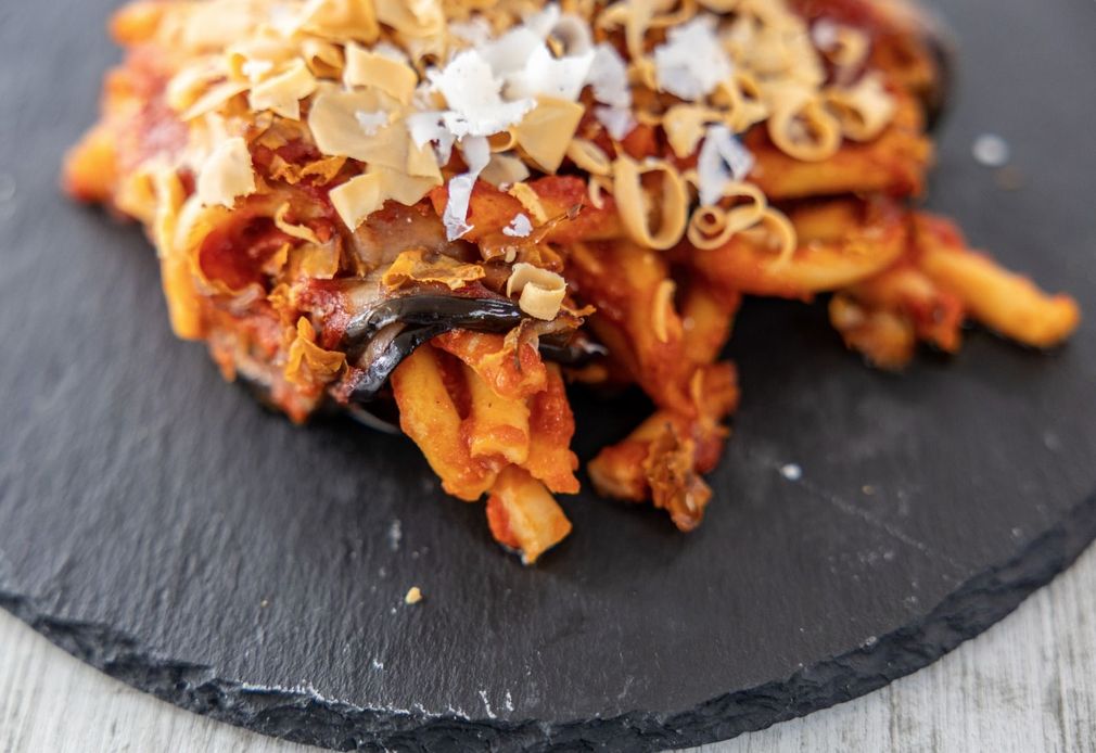 Pasta al sugo di pomodoro e scaglie di formaggio su un piatto di ardesia nera.
