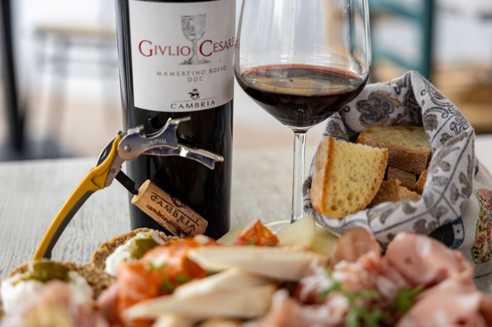 Una bottiglia di vino, un bicchiere e un tagliere di formaggi con pane e salumi su un tavolo.