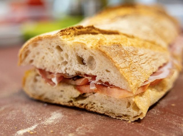 Primo piano di un panino croccante con prosciutto e formaggio fuso su un tagliere di legno.