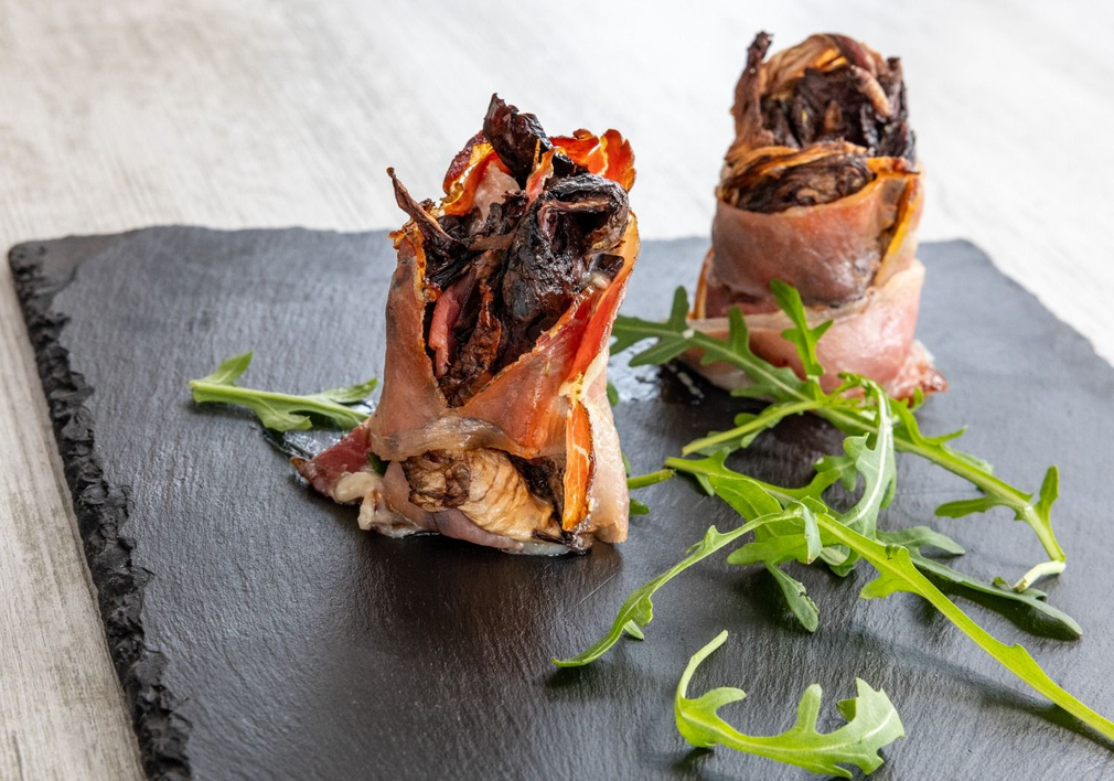 Due bocconcini ripieni di antipasto serviti su un'ardesia nera, guarniti con foglie di rucola.
