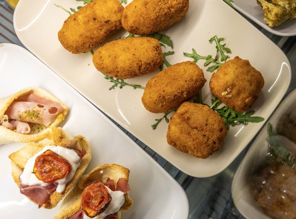 Piatto di crocchette fritte dorate con pasticcini salati in bocconcini, servite su piatti da portata bianchi.