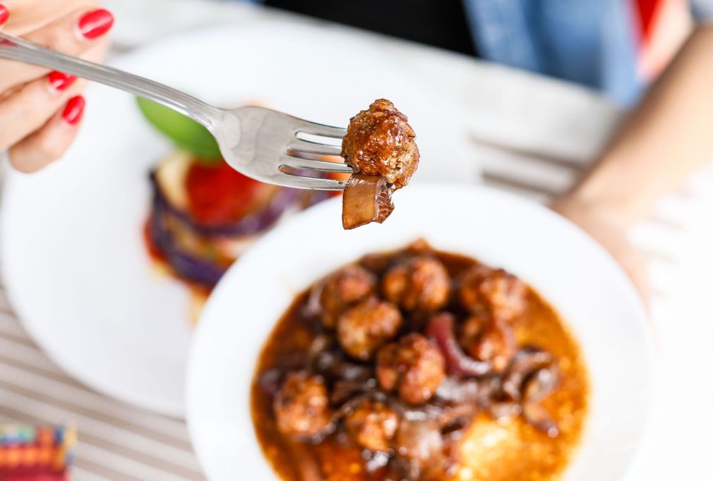 Sollevare una polpetta con la forchetta da una ciotola di pasta al sugo o di stufato
