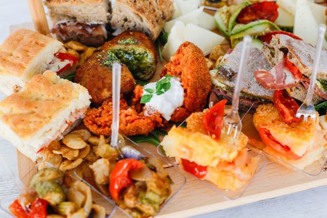 Un assortimento di antipasti e stuzzichini serviti su un vassoio di legno, tra cui panini, salsa di spinaci, patatine e spiedini.