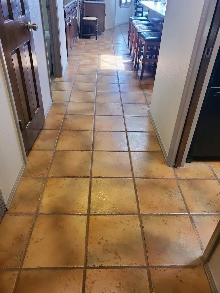 Narrow hallway with tan tile floor leading to a dining area and kitchen cabinets