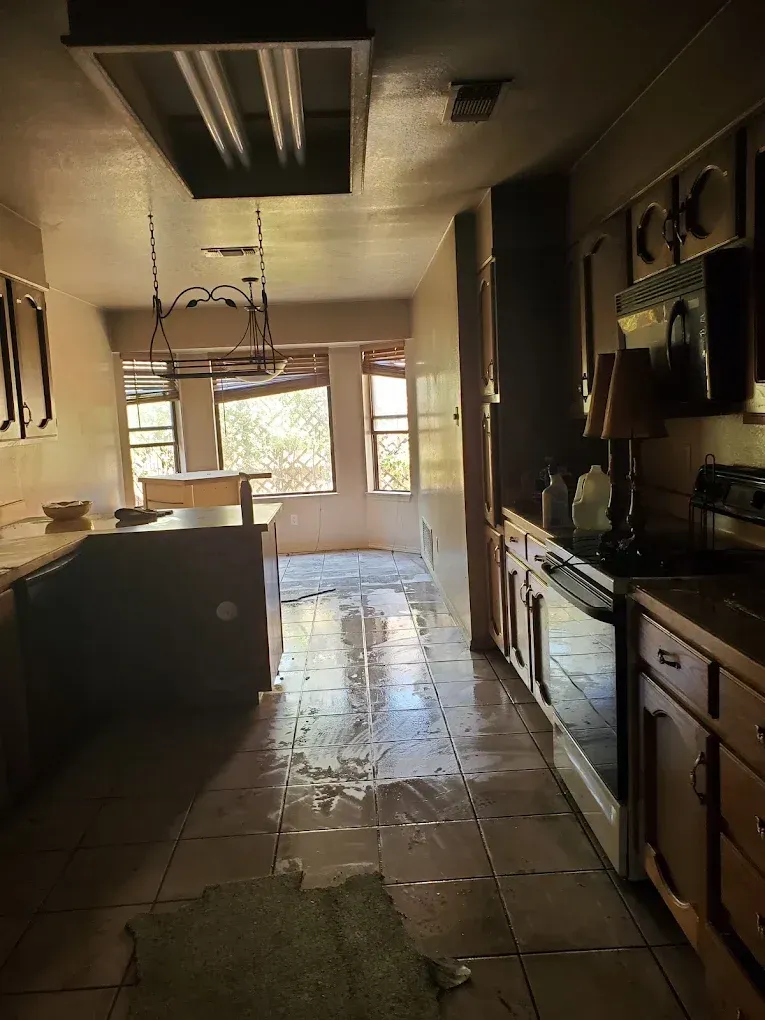 Dim kitchen with dark cabinets, tile floor, island, and sunlight through windows.