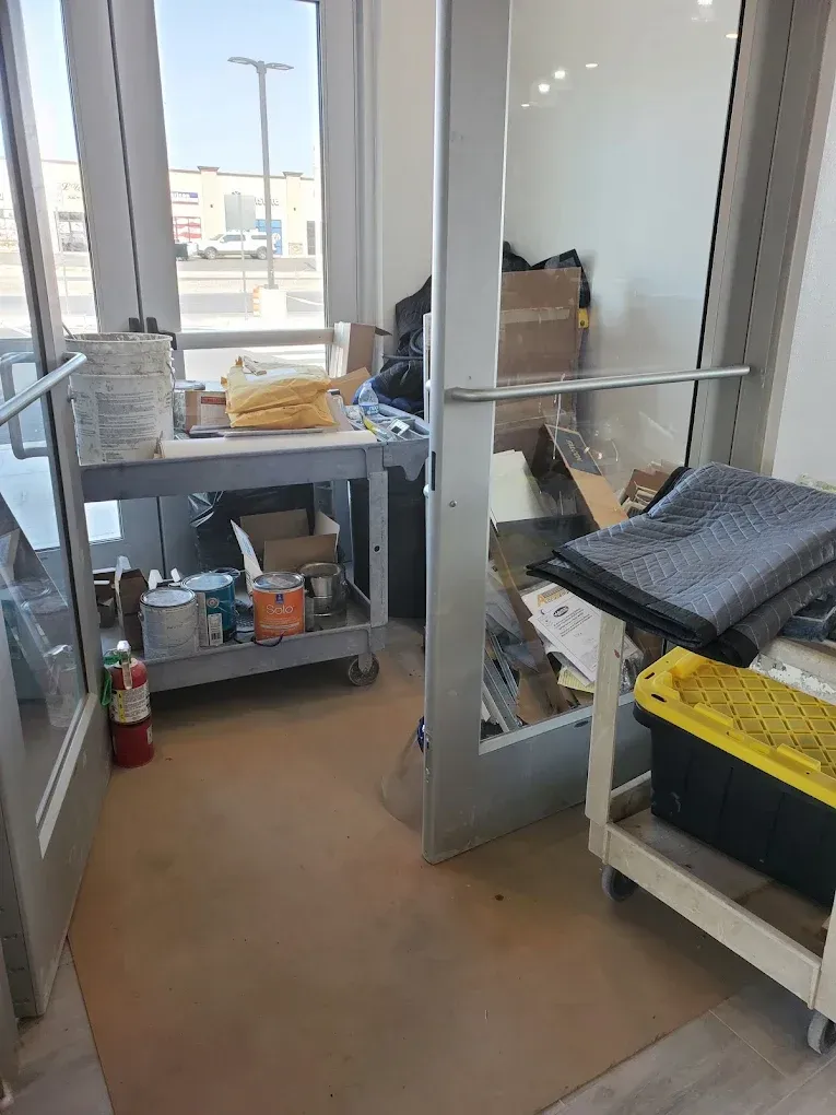 Indoor workspace with glass doors, a metal cart of supplies, and a yellow bin near a window.