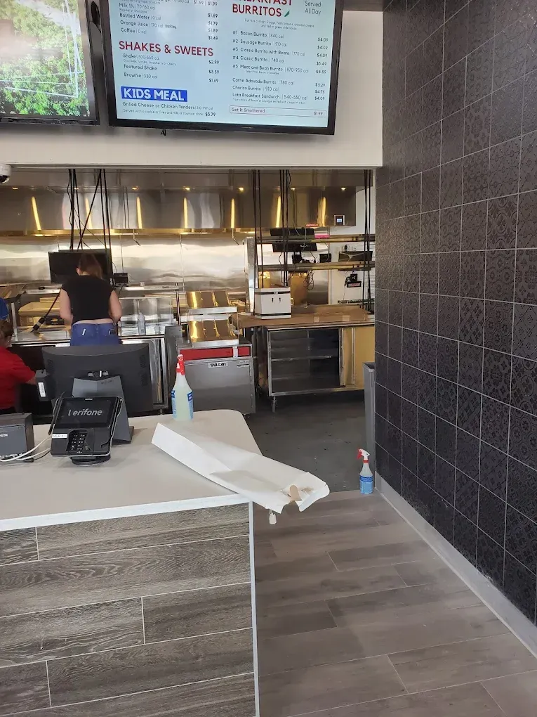 Fast-casual restaurant counter with menu boards, register, and open kitchen behind the counter.