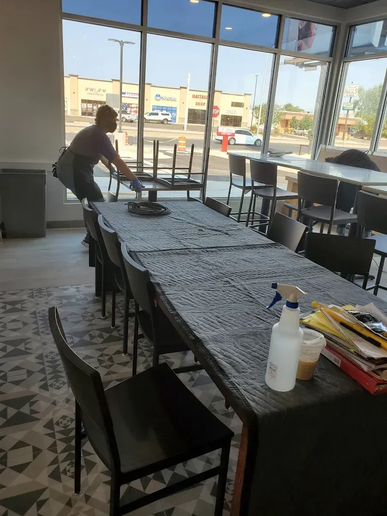 Person setting up a table in a bright café with large windows and a view outside