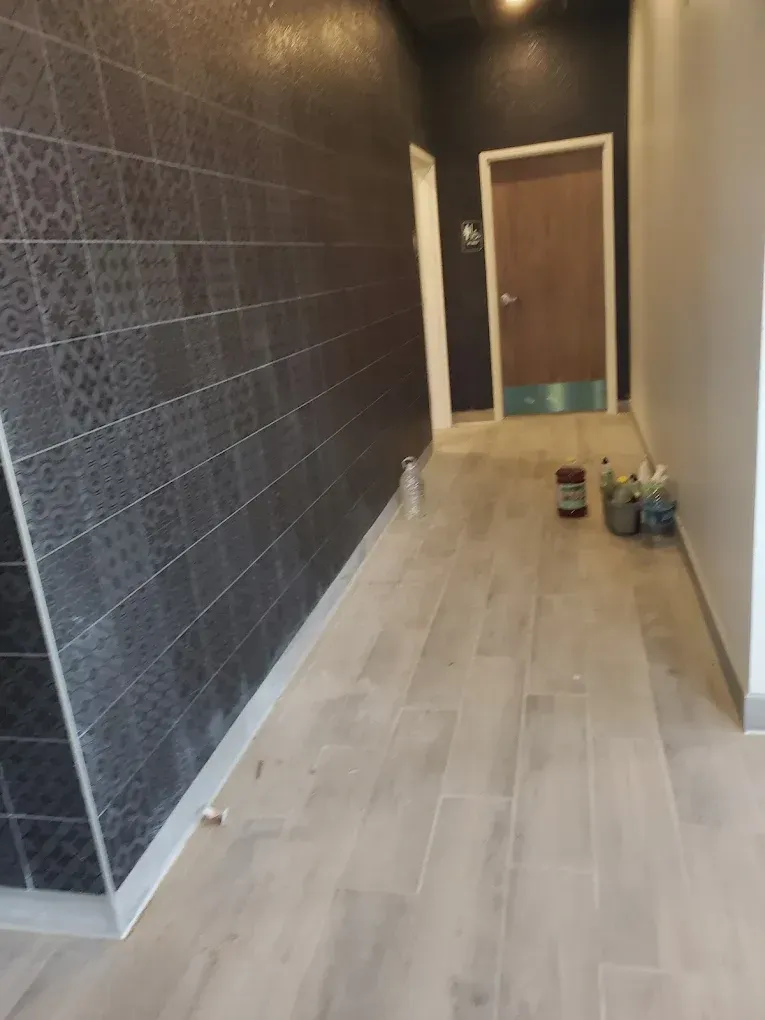 Narrow hallway under construction with dark walls, light wood floor, and tools near a door.