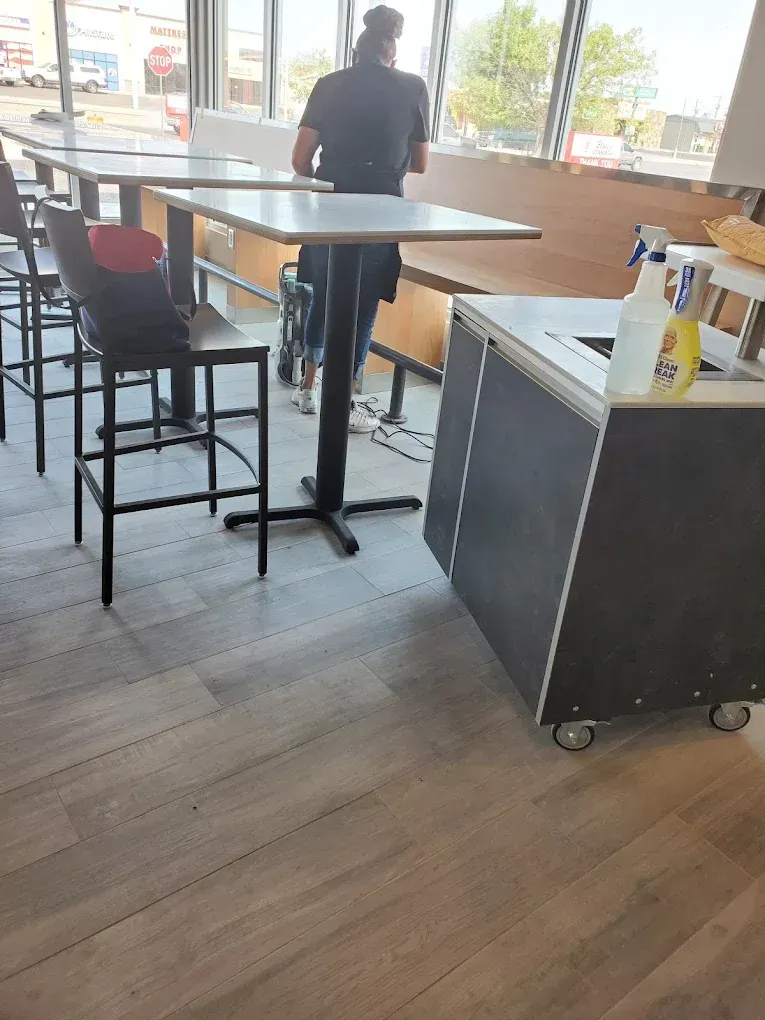 Person standing in a café near a high table, chair, and wheeled cart by the windows.