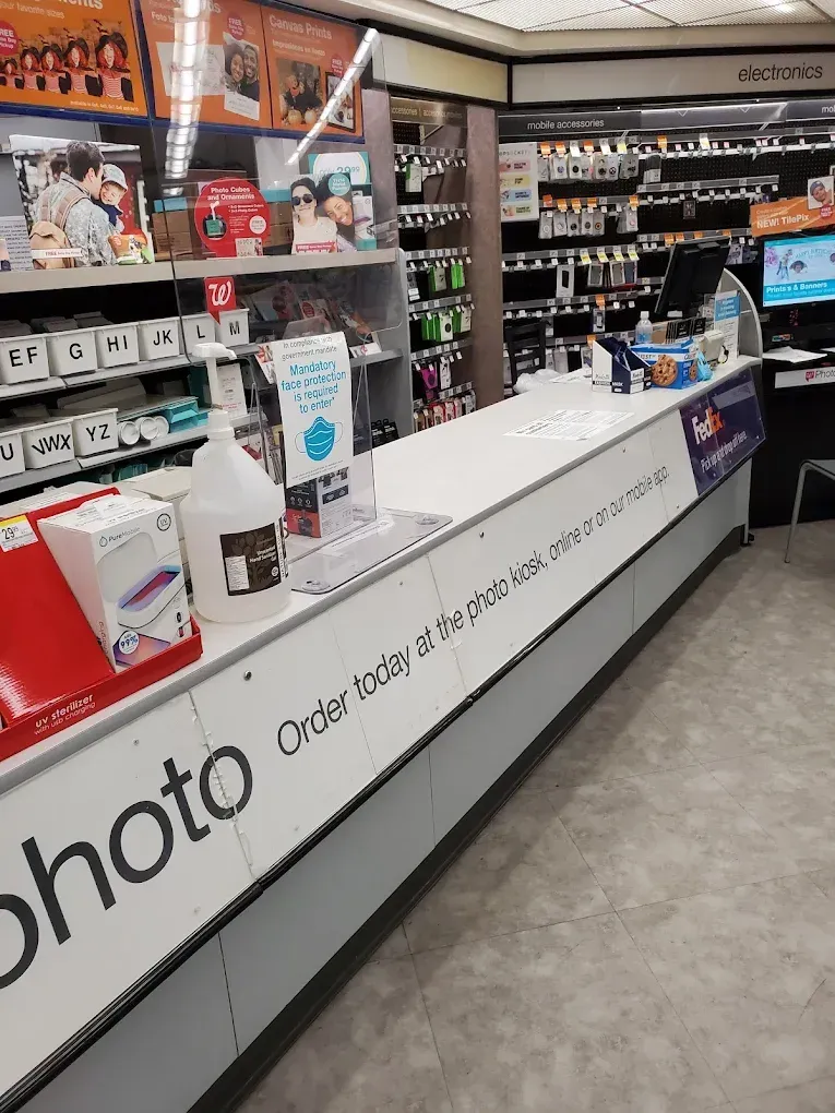 Photo counter with printers, cameras, and supplies in a retail store aisle.