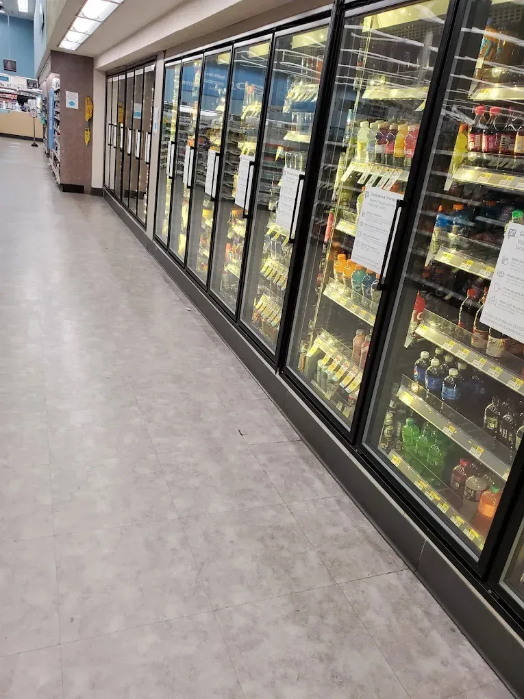 Store aisle with glass-doored refrigerated cases and products inside along a long hallway.