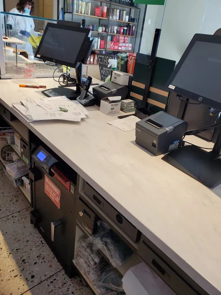 Retail checkout counter with two monitors, a receipt printer, and papers on a white countertop