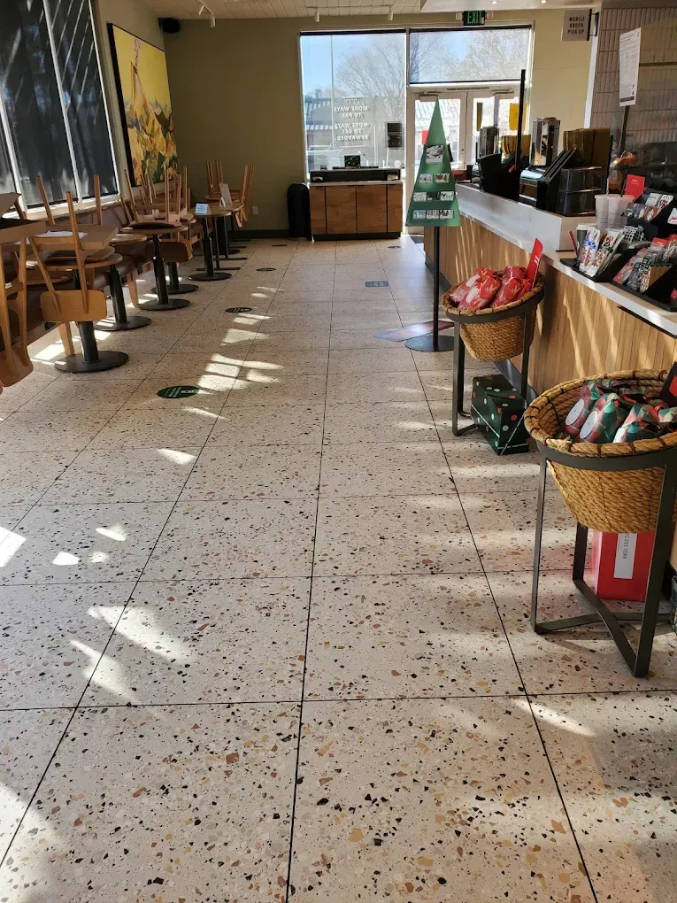 Empty café interior with sunlight on tiled floor, tables along the left, and baskets of snacks by the counter.