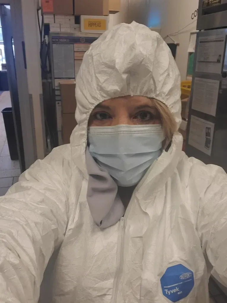 Person in white protective suit and face mask taking a selfie in a hallway.