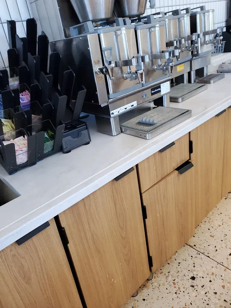 Coffee bar with an espresso machine, cups, and organizers on a countertop with wooden cabinets below