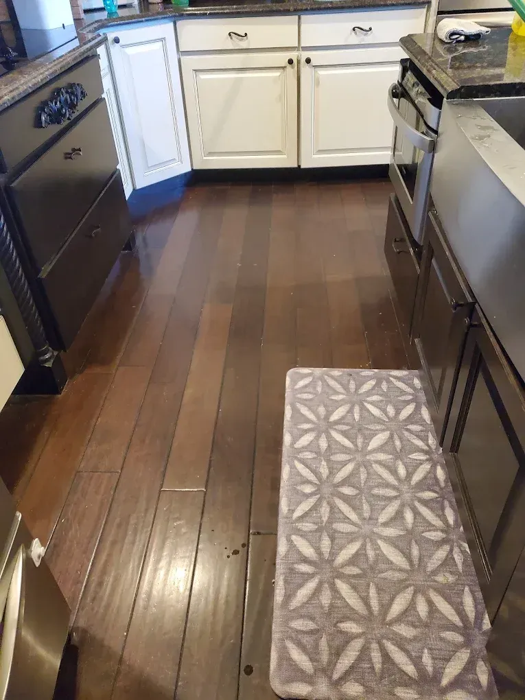 Narrow kitchen with dark wood floors, white cabinets, and a patterned rug near the stove and sink.