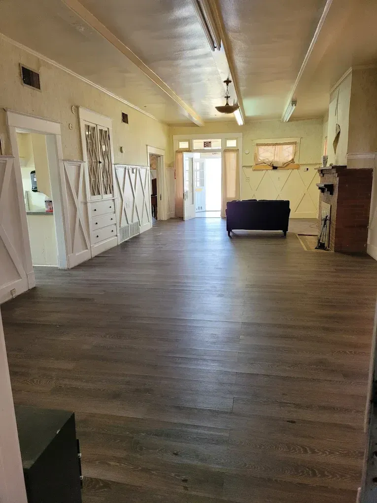 Empty hall with wood floors, white walls, open doors, and a black sofa near the back.