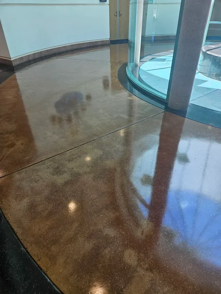 Polished brown lobby floor beside a curved glass entrance with reflections of lights and columns
