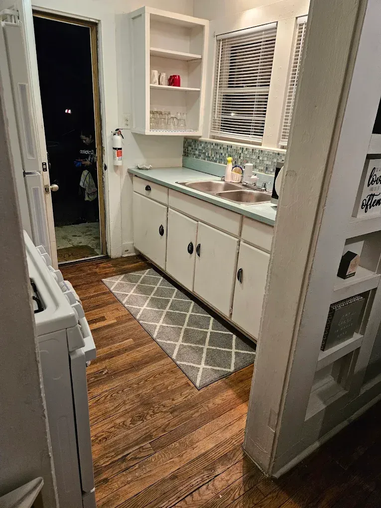 Small bathroom with white cabinets, wood floor, gray rug, sink vanity, and open doorway.
