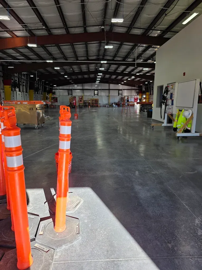 Interior of a warehouse under construction with orange safety cones and workers in high-visibility vests.