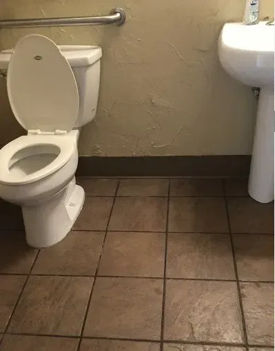 Accessible bathroom with a toilet, wall-mounted sink, and brown tiled floor.