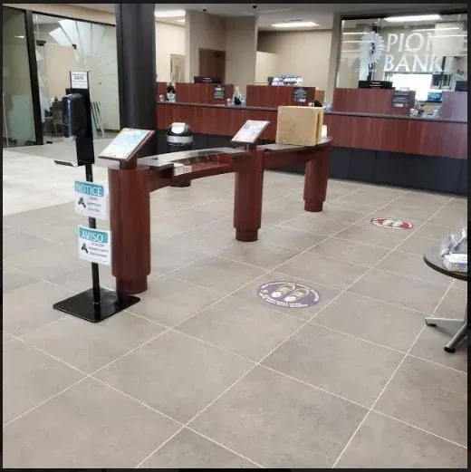 Bank lobby with a wooden checkpoint table, social distancing floor markers, and service counters in back.