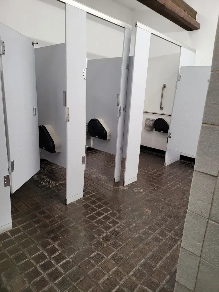 Public restroom with white stalls, dark tiled floor, and open stall doors.