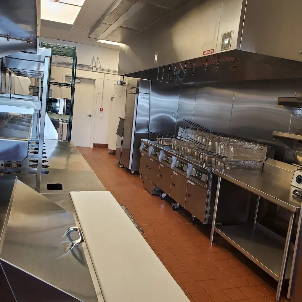 Commercial kitchen with stainless steel counters, ovens, and racks on a tiled floor
