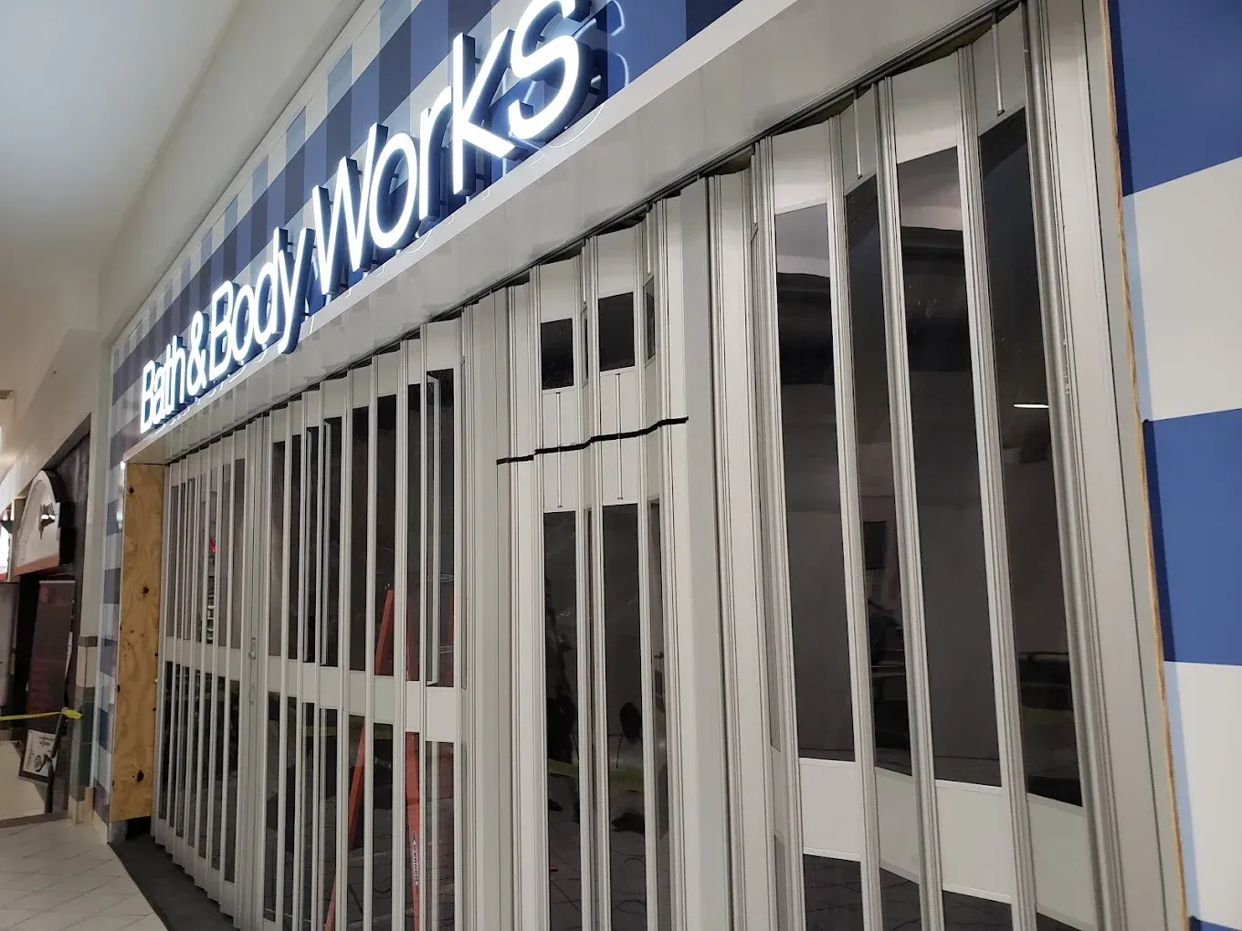 Barricaded Bath & Works storefront with metal gate down in a mall corridor