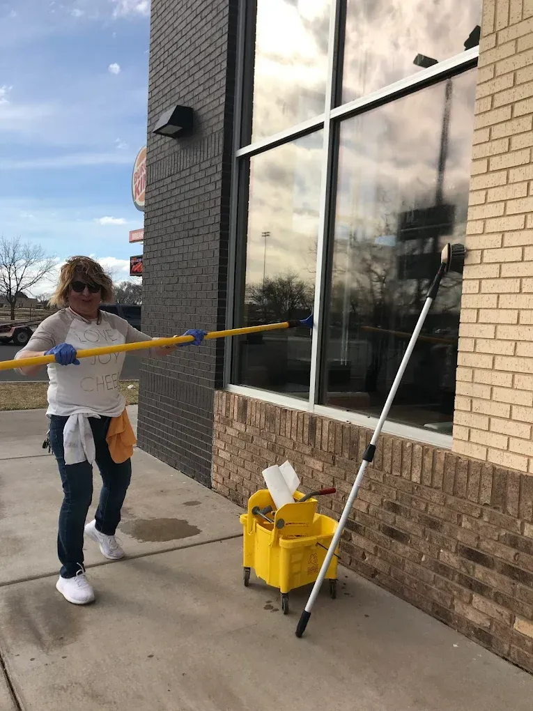 Person cleaning a storefront window with a squeegee beside a yellow cleaning cart