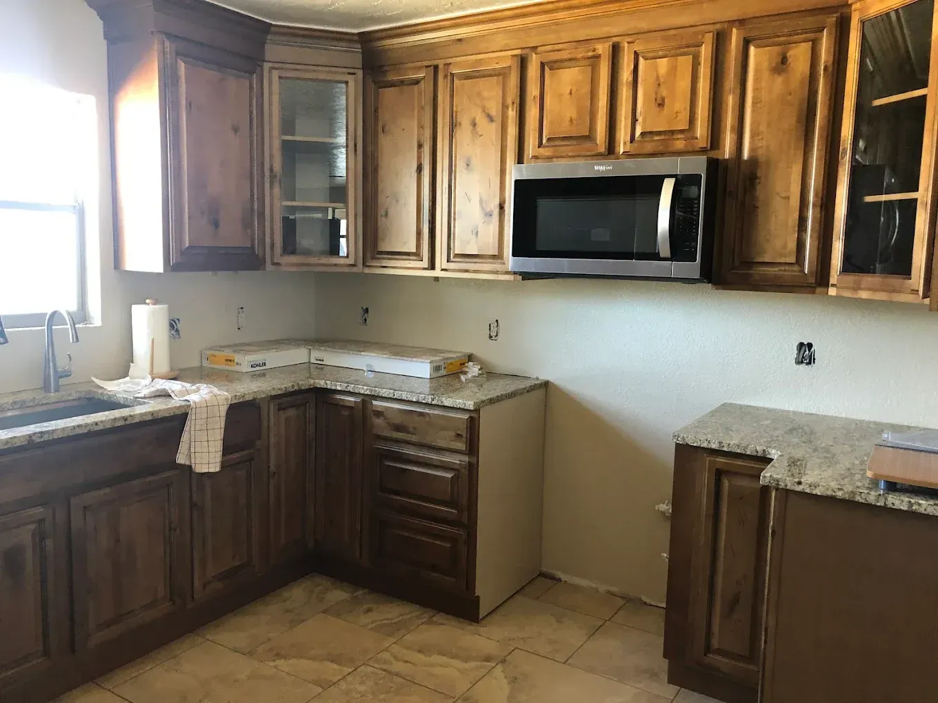 Empty kitchen with dark wood cabinets, granite countertops, and a stainless steel microwave.