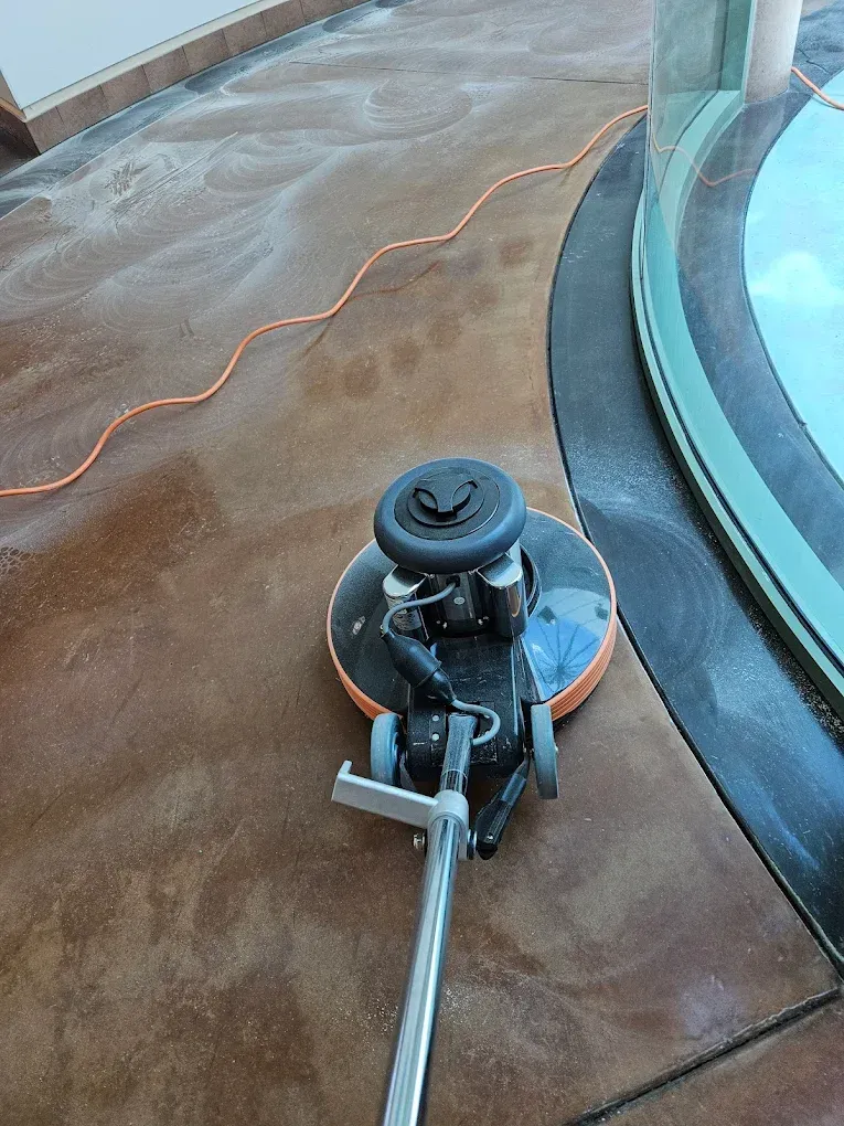 Floor polisher on a wet brown pool deck beside a blue hot tub, with an orange power cord attached