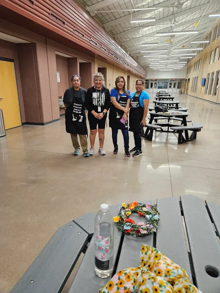 Four people standing in a bright hallway with picnic tables and a bouquet on a nearby table
