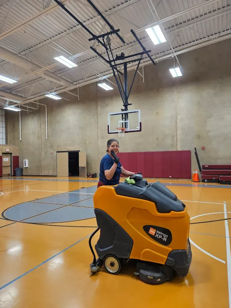 Person on a yellow floor-cleaning machine in a gymnasium