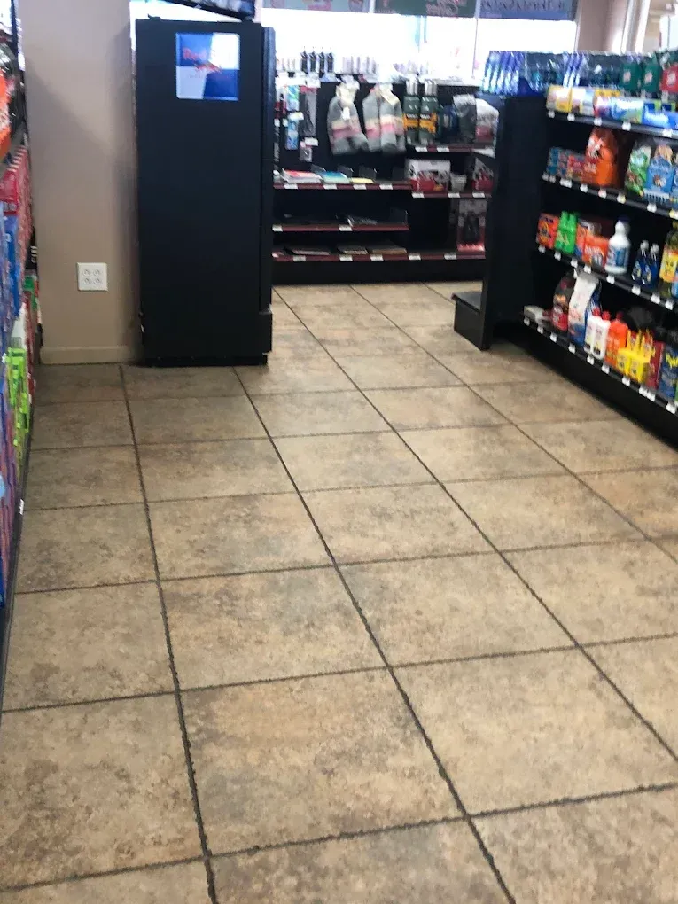 Convenience store aisle with tiled floor, refrigerated case, and shelves stocked with snacks and drinks